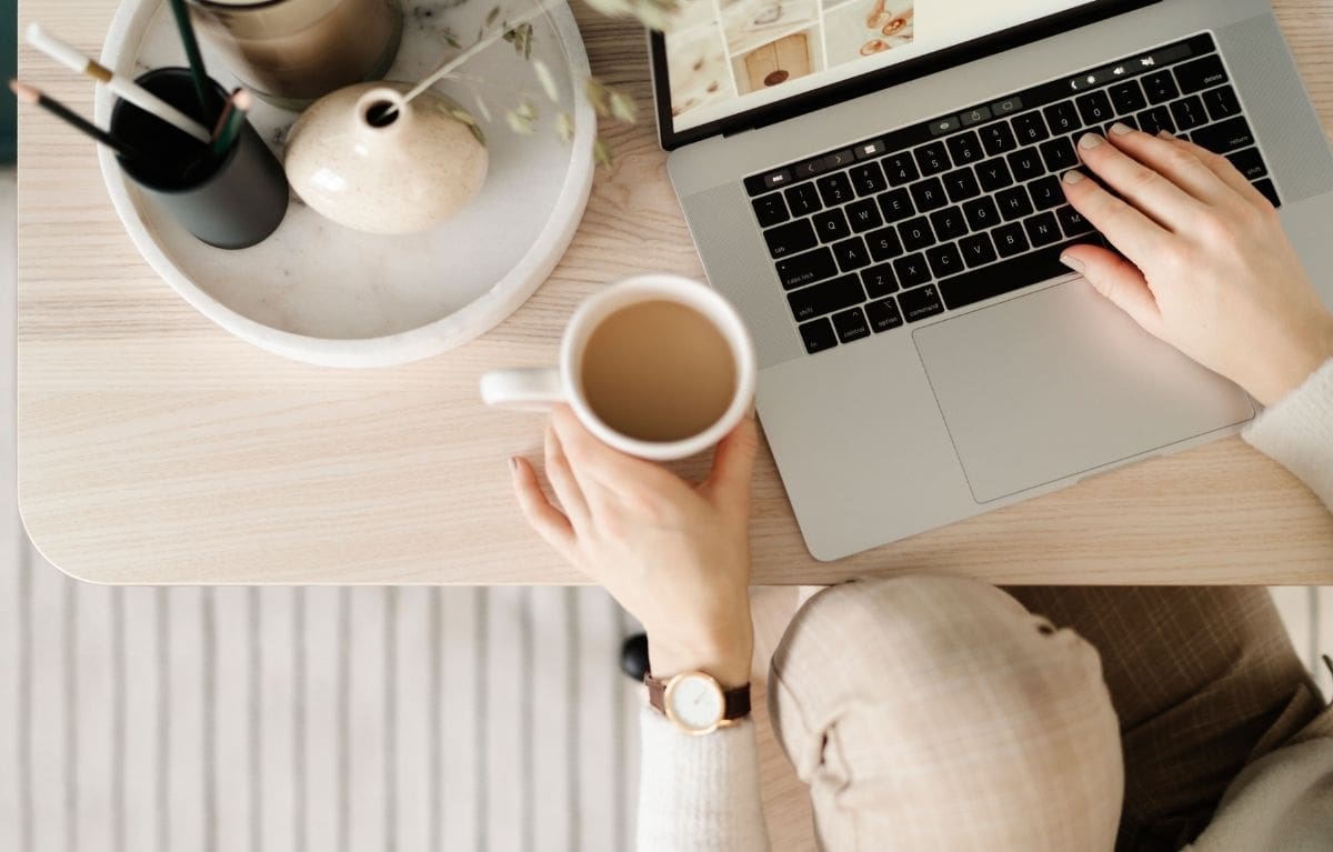 Hands typing on a laptop showing a grid of design inspiration images, with coffee and a ceramic tray on the desk