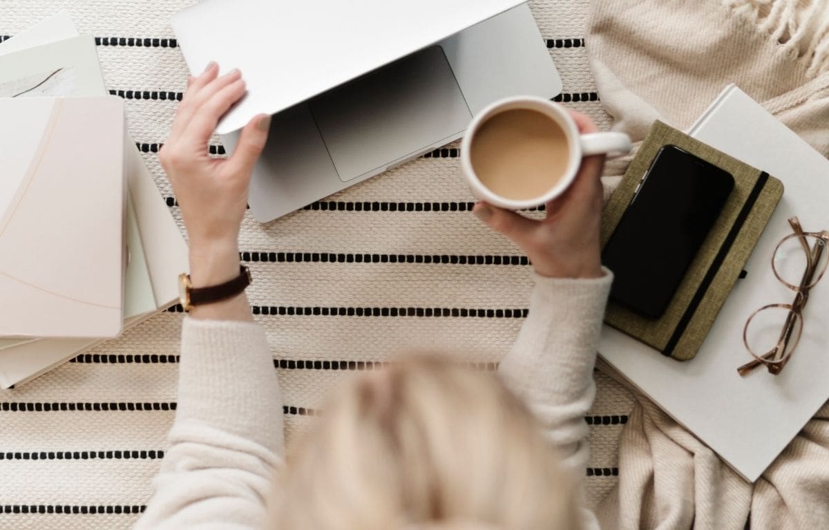 Interior designer closing her laptop with a cup of coffee in hand after finishing her website prep